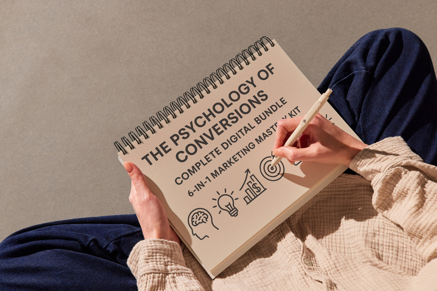 Person holding a notebook titled 'The Psychology of Conversions' with a pen.